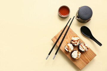 Tasty sushi rolls with chopsticks, teapot and cup of tea on light yellow background