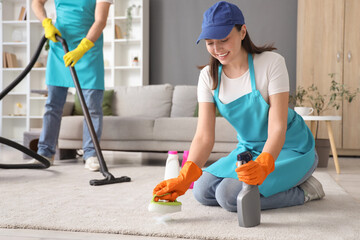 Female janitor cleaning carpet with brush in room
