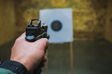 Tactical shooting from a pistol with a red dot sight at a target in a shooting range.