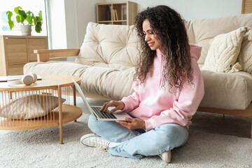 Obraz premium Young African-American woman with laptop resting on floor at home