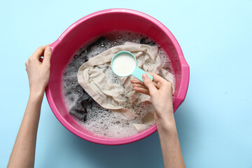 Woman adding laundry detergent to clothes in plastic basin on blue background