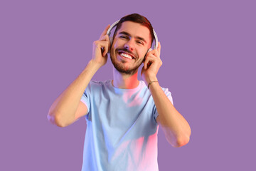 Young bearded man in headphones listening to music on lilac background