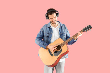 Obraz premium Young bearded man in headphones playing guitar on pink background