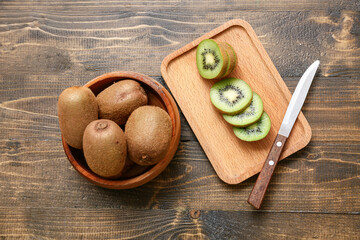 Bowl and board with fresh kiwi on wooden background