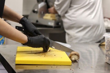 Hands cutting mushrooms in a restaurant kitchen with another person in the background