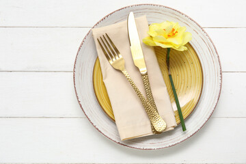 Stylish table setting with golden cutlery and beautiful flower on white wooden background