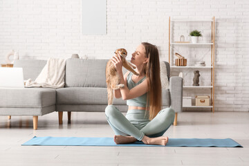 Young woman with cute kitten sitting on yoga mat at home