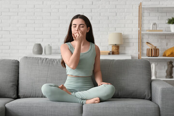 Pretty young woman doing breath practice on sofa at home