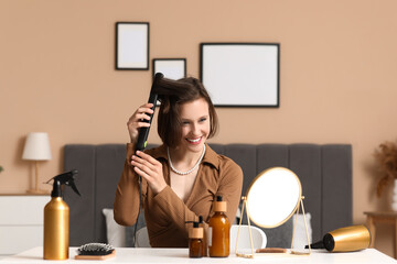 Beautiful young happy woman with curling iron and hair care products at home