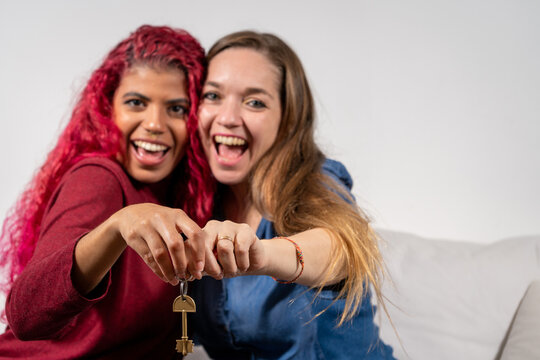Pareja de mujeres sosteniendo una llave a c&aacute;mara en se&ntilde;al de felicidad por adquirir su primera casa