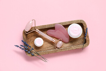 Jade roller with gua sha, cosmetic cream and lavender on pink background
