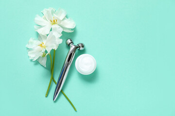 Facial roller with cosmetic cream and beautiful flowers on turquoise background