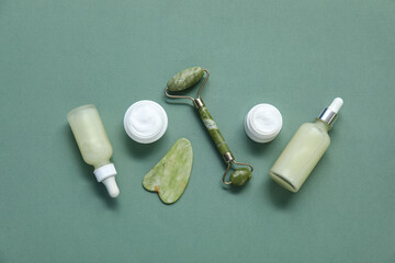 Jade roller with gua sha, serum and cosmetic cream on green background