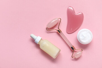 Jade roller with gua sha, seruma and cosmetic cream on pink background