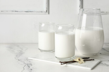 Glasses and jug of fresh vanilla milk with sticks and flower on white background