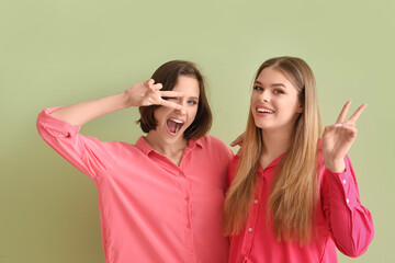 Female friends showing victory gesture on green background