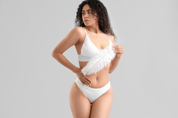 Obraz premium Young African-American woman in underwear with feather on light background