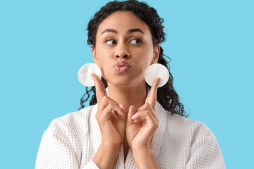 Young African-American woman with cotton pads blowing kiss on blue background, closeup