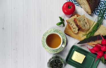 Widok z góry na pyszne domowe śniadanie: świeżo upieczony chleb, masło, szczypior, pomidor i zielona herbata © KJP Photography