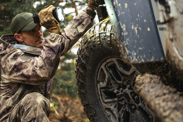 Man Inspecting Mud-Covered Tire in Forest