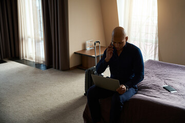 African american businessman talking on phone and using laptop in hotel room