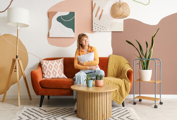 Young woman sitting on sofa with hanging stylish paintings at home