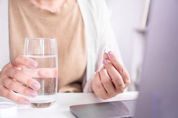closeup woman hand taking paracetamol medicine with a glass of water to relief headache, cold and...
