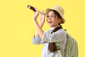 Cute little tourist looking through spyglass on yellow background