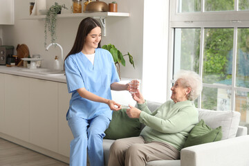 Young nurse giving pills and glass of water to senior woman in kitchen