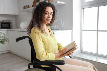 Young African-American woman in wheelchair reading book at home