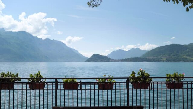 Railing with flower pots and bench with blurry mountains of lake como italy