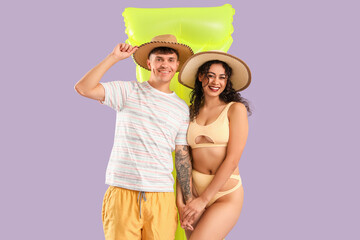Happy young couple with inflatable mattress on lilac background