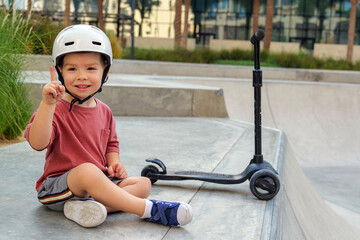 Obraz premium little boy wearing a helmet and with his scooter in a skate park