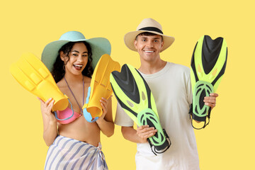 Happy young couple with flippers on yellow background
