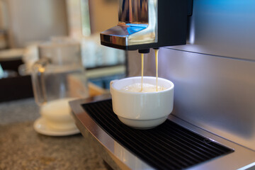 A coffee machine is pouring milk into a white cup.