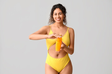 Beautiful young African-American woman in stylish yellow swimsuit with bottle of sunscreen cream on...