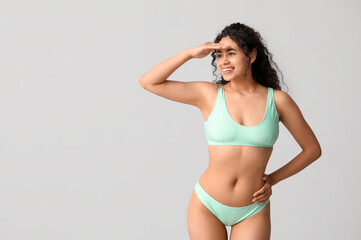 Beautiful young African-American woman in stylish turquoise swimsuit on grey background