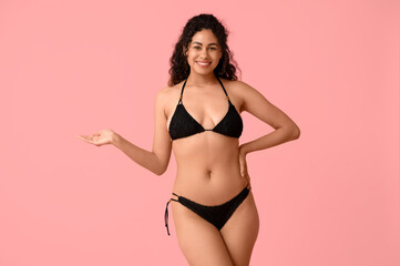 Beautiful young African-American woman in stylish black swimsuit on pink background