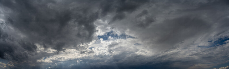 Wide panorama of a sky full of storm clouds with a small area of blue sky. A rainstorm is brewing
