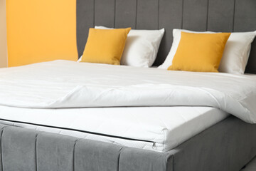 New orthopedic mattress with blanket on stylish bed near yellow wall in room, closeup