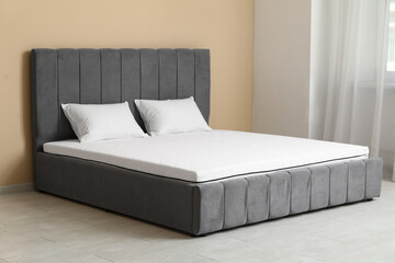 New orthopedic mattress on stylish bed near beige wall in room