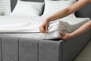 Woman with soft orthopedic mattress making bed at home, closeup