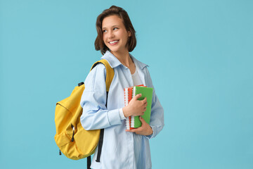 Beautiful female student with backpack and notebooks on blue background