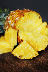 Ripe juicy pineapple next to cut pieces on a wooden board on a dark background