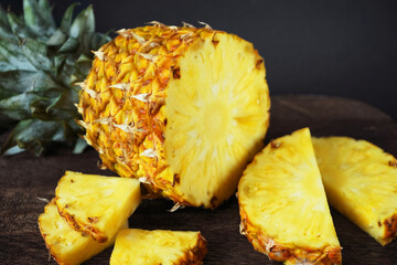 Ripe juicy pineapple next to cut pieces on a wooden board on a dark background