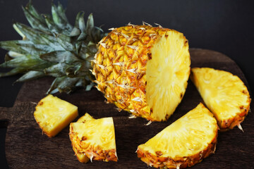 Ripe juicy pineapple next to cut pieces on a wooden board on a dark background