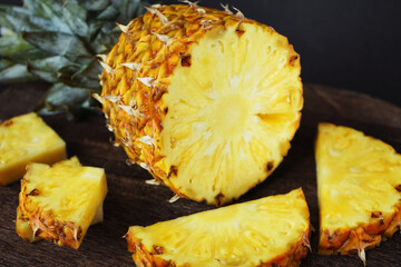 Ripe juicy pineapple next to cut pieces on a wooden board on a dark background