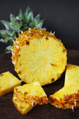 Ripe juicy pineapple next to cut pieces on a wooden board on a dark background