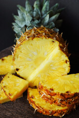Ripe juicy pineapple next to cut pieces on a wooden board on a dark background