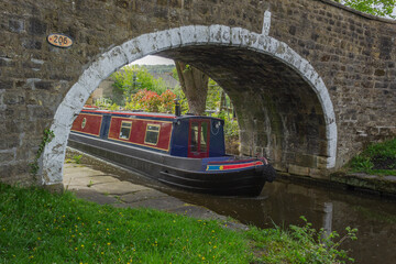 A colourful canal boat emerges from under an old stone bridge on the Leeds and Liverpool Canal as it makes its way through Yorkshire